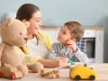 Uśmiechnięta opiekunka karmi chłopca. Zastanawiasz się, ile płaci się opiekunce do dziecka za taką troskę?