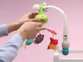 Ręce montują karuzelę podróżną Tiny Love z kolorowymi zabawkami.