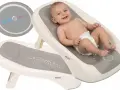 Uśmiechnięty niemowlak w pieluszce leży na leżaczku do kąpieli dla niemowlaka. Produkt BabyMam zapewnia bezpieczeństwo i komfort podczas kąpieli.