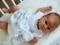 Uroczy noworodek w białym body i otulony wzorzystym kocykiem. Czy to pieluszki muślinowe czy bambusowe? Delikatność dla maluszka.