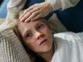 Dziecko z gorączką leży na poduszce, a ręka mamy sprawdza mu czoło. Czy dziecko z gorączką może wychodzić na dwór?