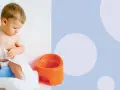 Małe dziecko siedzi na niebieskim nocniku, bawiąc się papierem toaletowym. Kiedy uczyć dziecko na nocnik? Czas zacząć!