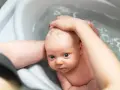 Niemowlę w wanience, myte przez rodzica. Czy można kąpać dziecko jak ma gorączkę? Woda może pomóc obniżyć temperaturę.