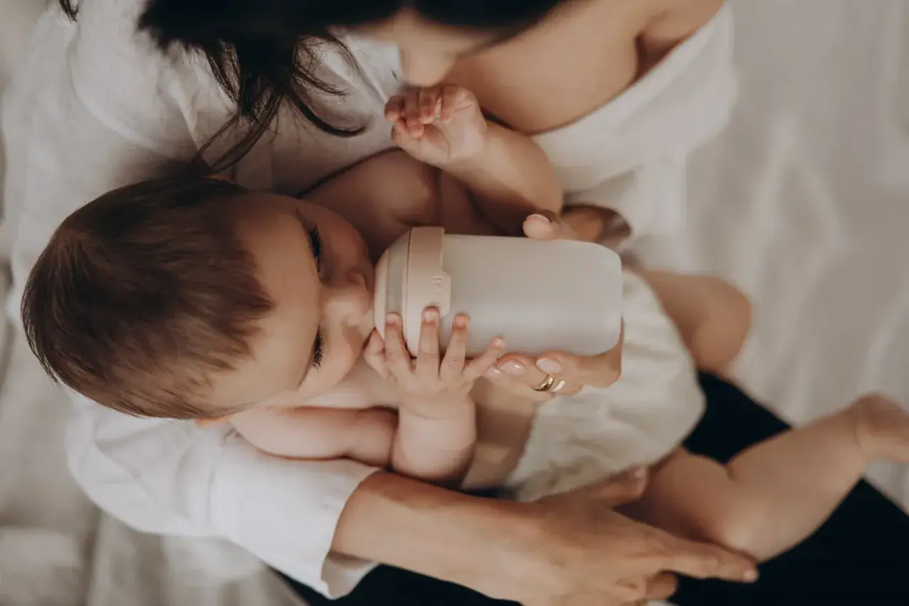 Dziecko pije z butelki przypominającej pierś. Mama czule trzyma butelkę, zapewniając maluchowi komfort.