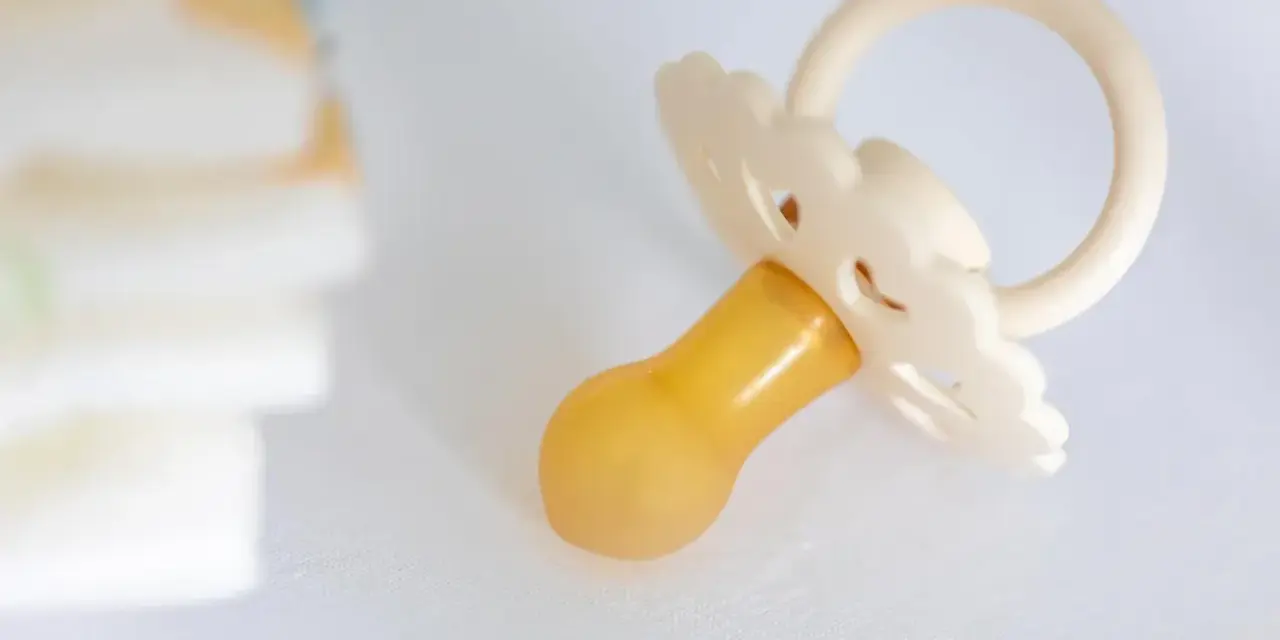 Smoczek przypominający pierś, obok stosu pieluch.