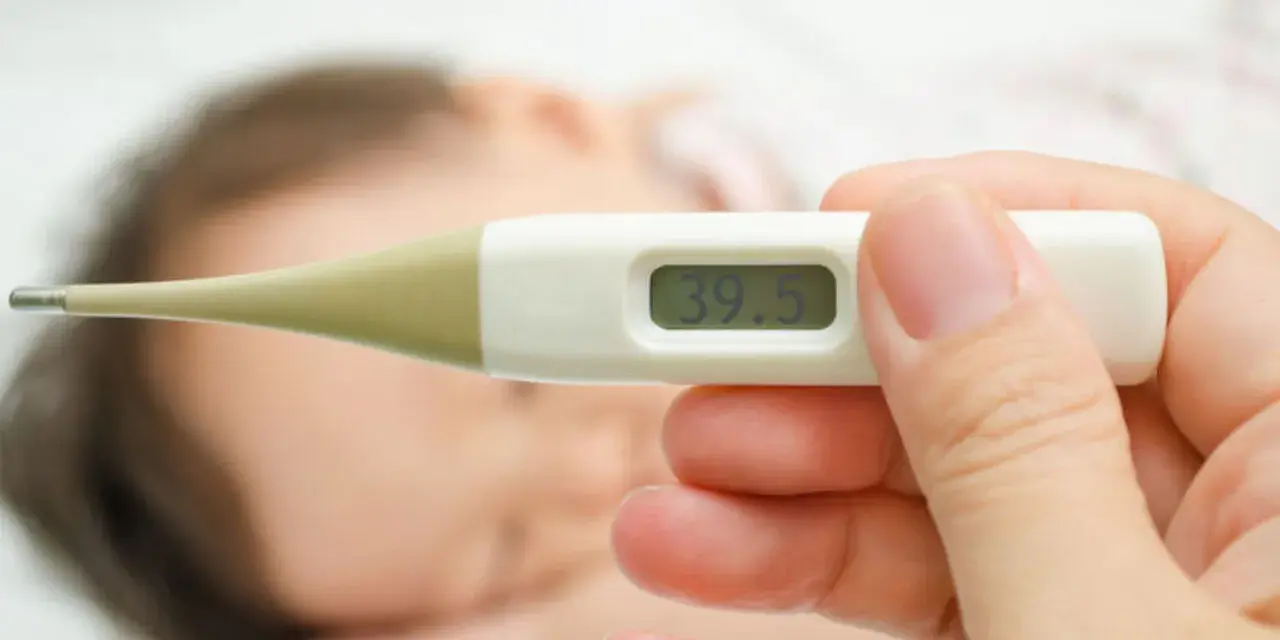 Cyfrowy termometr pokazuje 39.5°C. W tle widać śpiące dziecko. Zastanawiasz się, ile czasu mierzyć temperaturę pod pachą?