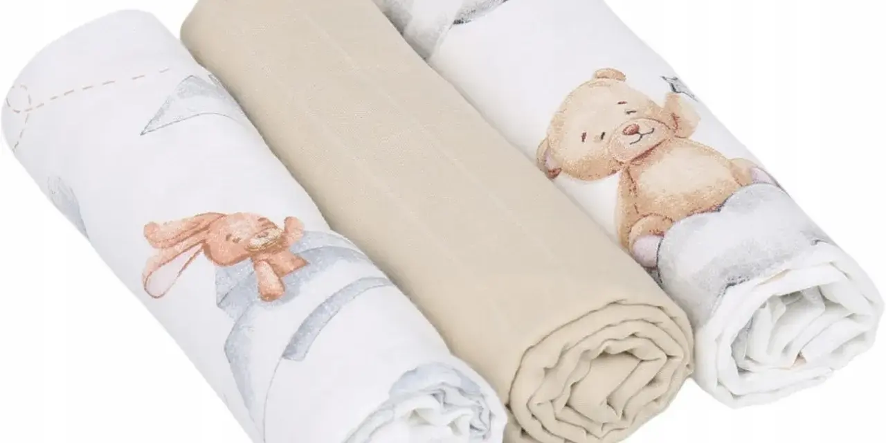 Trzy zwinięte babyono pieluszki muślinowe: dwie z motywem misia i królika, jedna gładka, beżowa.