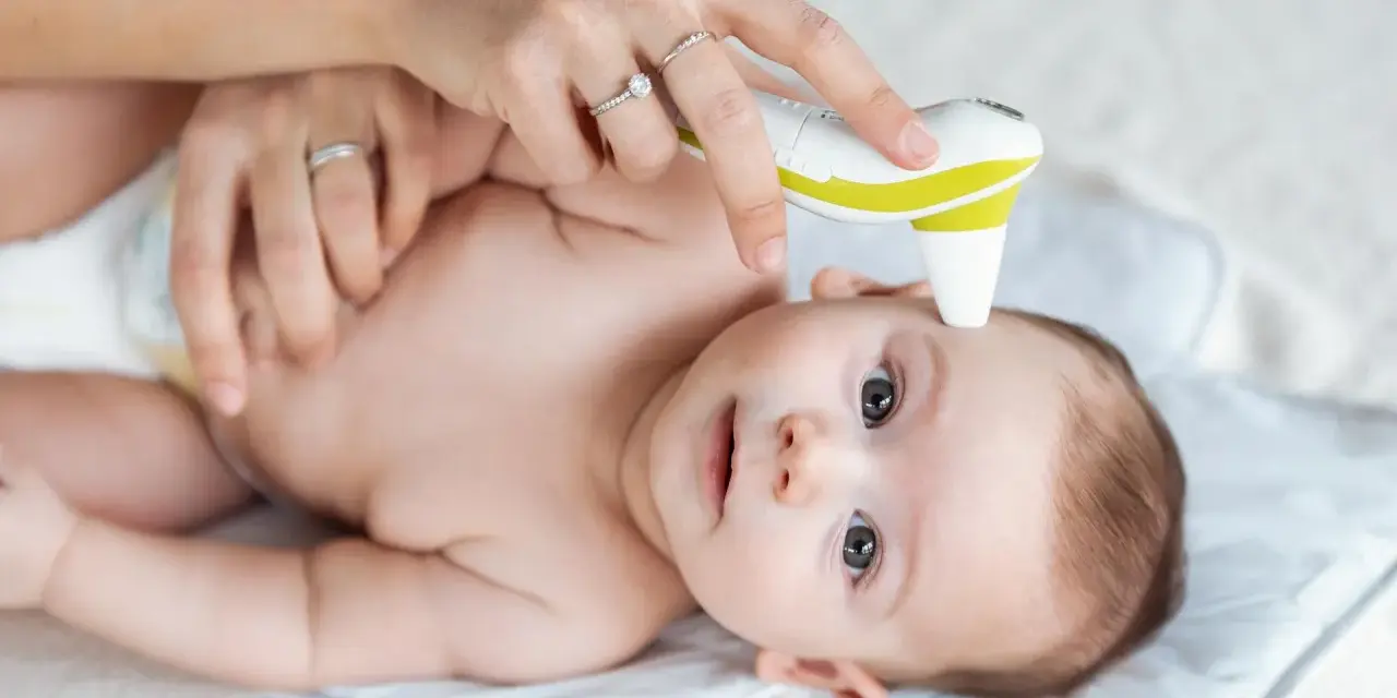 Mama mierzy temperaturę czoła niemowlaka termometrem bezdotykowym. To szybki sposób, gdzie mierzyć temperaturę u niemowlaka.