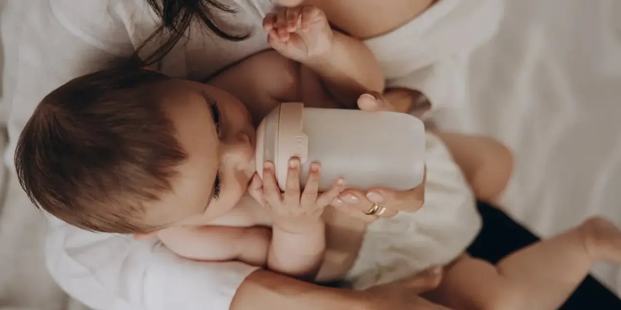 Dziecko pije z butelki przypominającej pierś. Mama czule trzyma butelkę, zapewniając maluchowi komfort.