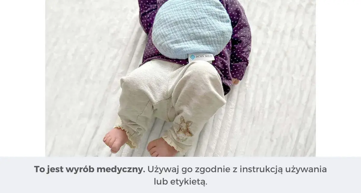 Niemowlę z termoforem z pestek na brzuszku. Delikatny, błękitny termofor z pestek wiśni ogrzewa maluszka.