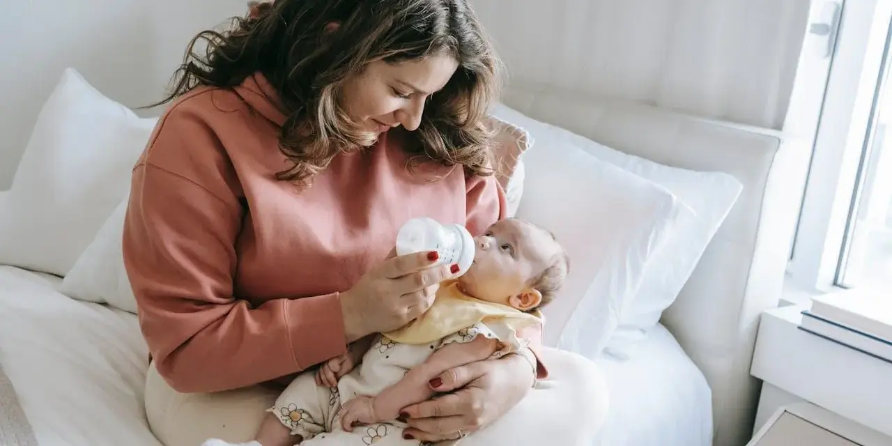 Mama karmi dziecko butelką, używając miarki do mleka modyfikowanego.