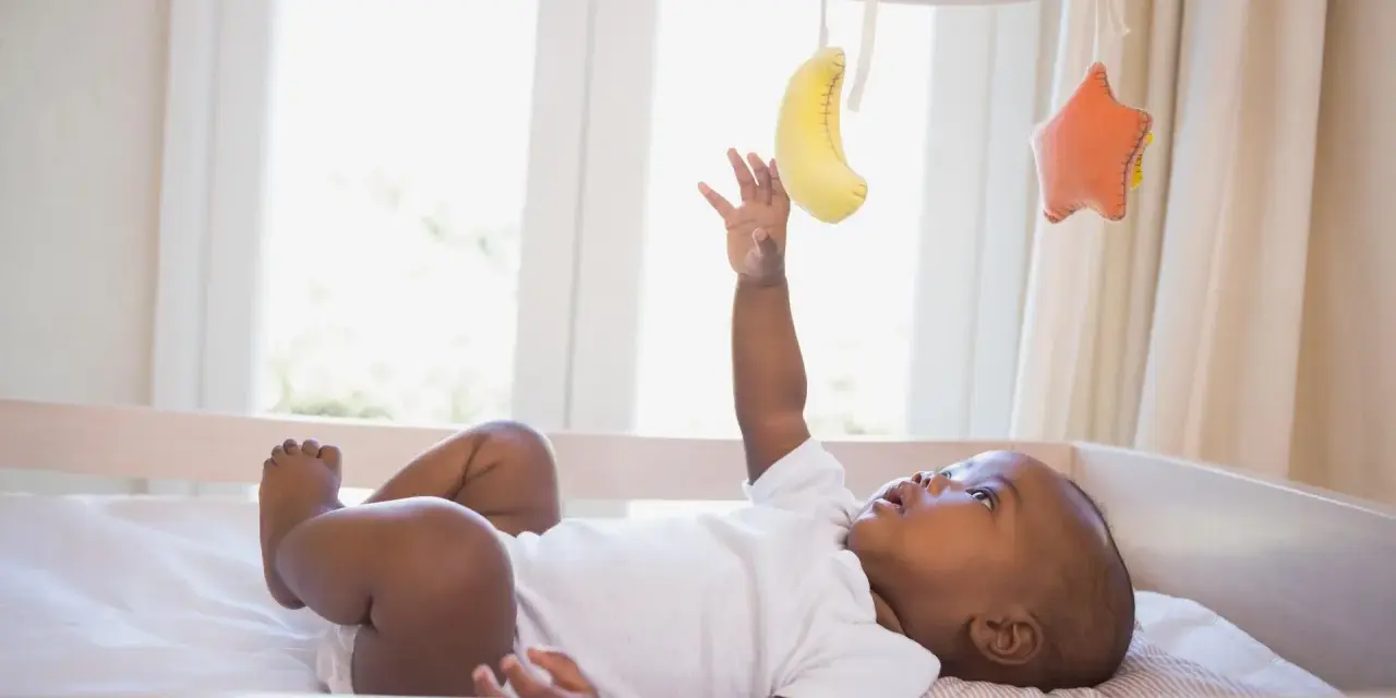 Niemowlę wyciąga rączkę do kolorowej karuzeli dla dzieci do łóżeczka z bananem i gwiazdką.