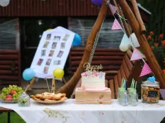 Na stole na roczek kładzie się tort, owoce, ciasteczka i słodkości. Dekoracje tworzą girlandy i zdjęcia.