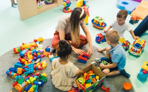 Dzieci bawią się klockami z opiekunką. Czy za żłobek się płaci? To pytanie zadają sobie rodzice, widząc radosne chwile swoich pociech.