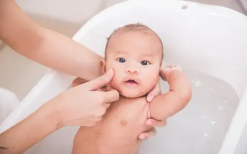 Delikatna kąpiel niemowlaka w wanience. Czy można myć dziecko z gorączką? Tak, ale w letniej wodzie, by pomóc mu się ochłodzić.