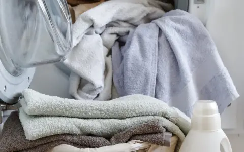 Pranie delikatnych ręczników dla dzieci. Obok pralki kosz z czystymi ręcznikami i butelka płynu do prania dla dzieci.