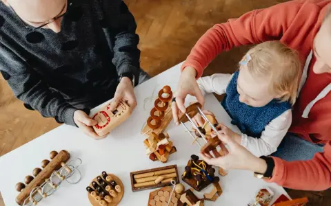 Rodzina bawi się drewnianymi łamigłówkami. Dziecko z rodzicami rozwiązuje zagadki, przygotowując się do przedszkola.
