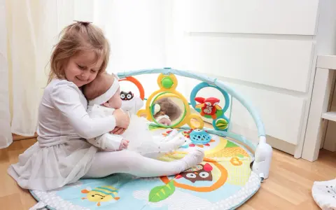 Starsza siostra tuli niemowlę na kolorowych matach interaktywnych dla dzieci, pełnych zabawek i lusterka.