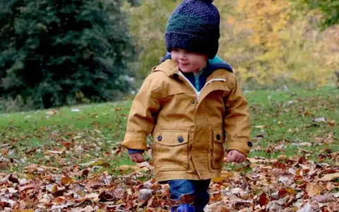 Mały chłopiec w jesiennej kurtce i czapce spaceruje po parku wśród opadłych liści. Idealne miejsce, gdzie na weekend z dzieckiem jesienią.