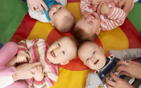 Uśmiechnięte dzieci na kolorowej macie. Czy żłobek jest dobry dla dziecka? Wiele maluchów wesoło bawi się z opiekunami.