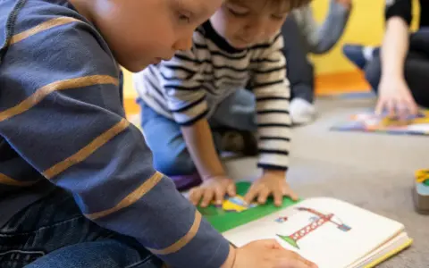 Dzieci uczą się i bawią razem, czytając książkę. To pokazuje, czy warto dać dziecko do żłobka.