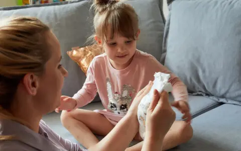 Mama pokazuje córce pieluchę, symbolizując etap, kiedy dziecko przestaje nosić pieluchy.
