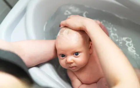 Niemowlę w wanience, myte przez rodzica. Czy można kąpać dziecko jak ma gorączkę? Woda może pomóc obniżyć temperaturę.