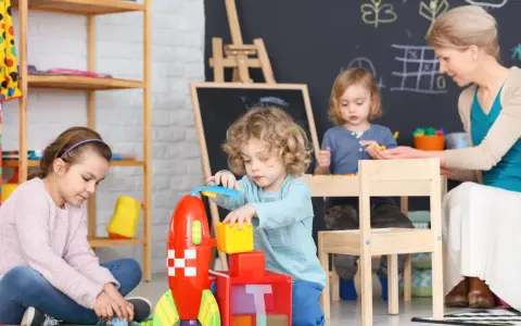 Dzieci budują rakietę z klocków, a opiekunka czuwa. Ciekawe, ile zarabia opiekunka w żłobku za taką pracę.