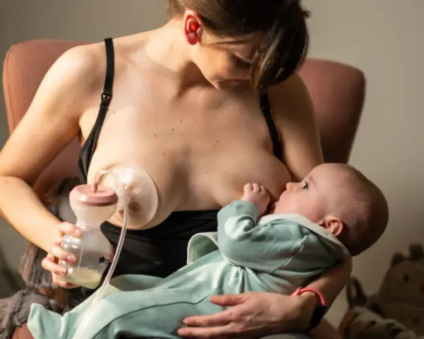 Kobieta karmi piersią dziecko, jednocześnie używając laktatora Tommee Tippee do odciągania mleka.