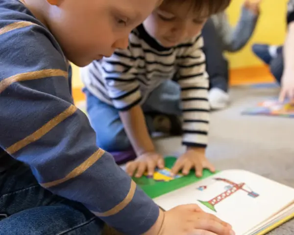 Dzieci uczą się i bawią razem, czytając książkę. To pokazuje, czy warto dać dziecko do żłobka.