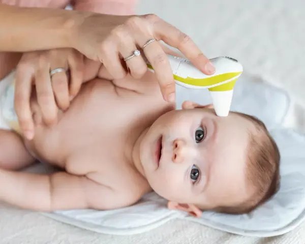 Mama mierzy temperaturę czoła niemowlaka termometrem bezdotykowym. To szybki sposób, gdzie mierzyć temperaturę u niemowlaka.