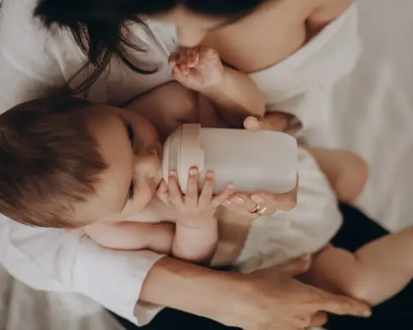 Dziecko pije z butelki przypominającej pierś. Mama czule trzyma butelkę, zapewniając maluchowi komfort.