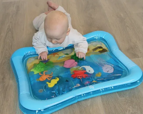 Niemowlę bawi się na dmuchanej macie wodnej z morskimi zwierzątkami. Kolorowa zabawka zachęca do odkrywania podwodnego świata.