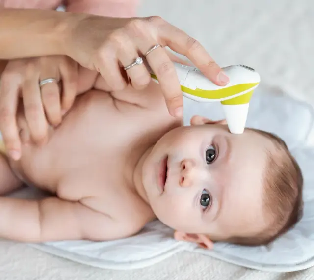 Mama mierzy temperaturę czoła niemowlaka termometrem bezdotykowym. To szybki sposób, gdzie mierzyć temperaturę u niemowlaka.