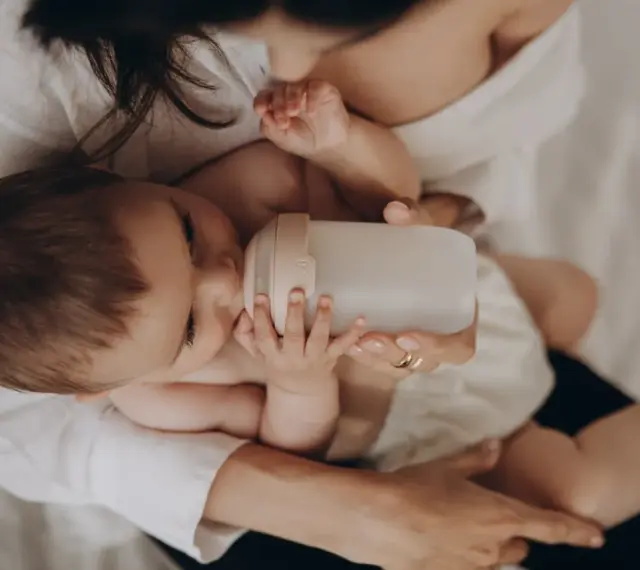 Dziecko pije z butelki przypominającej pierś. Mama czule trzyma butelkę, zapewniając maluchowi komfort.