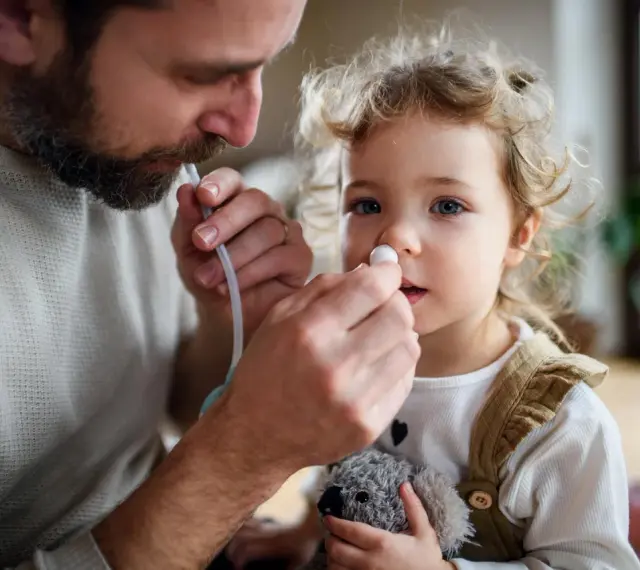 Tata delikatnie używa odkurzacza do nosa dla niemowląt, pomagając dziecku oddychać swobodniej.