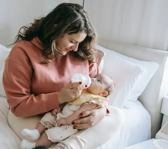 Mama karmi dziecko butelką, używając miarki do mleka modyfikowanego.