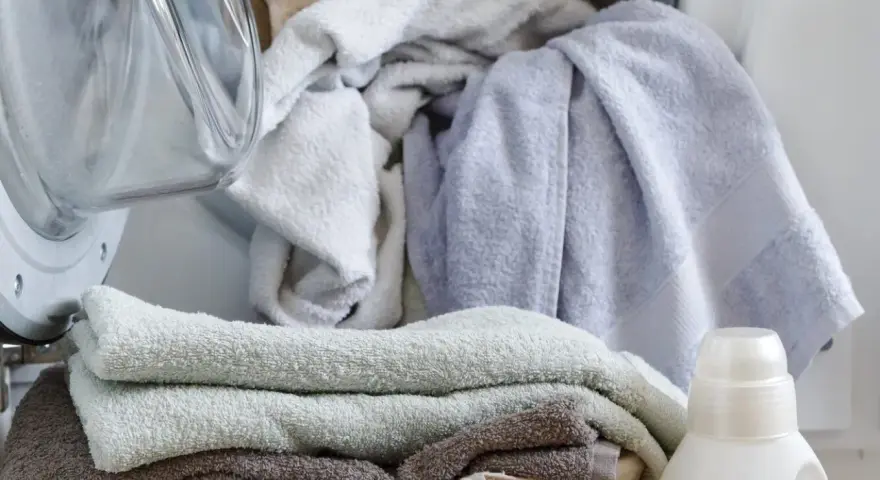 Pranie delikatnych ręczników dla dzieci. Obok pralki kosz z czystymi ręcznikami i butelka płynu do prania dla dzieci.