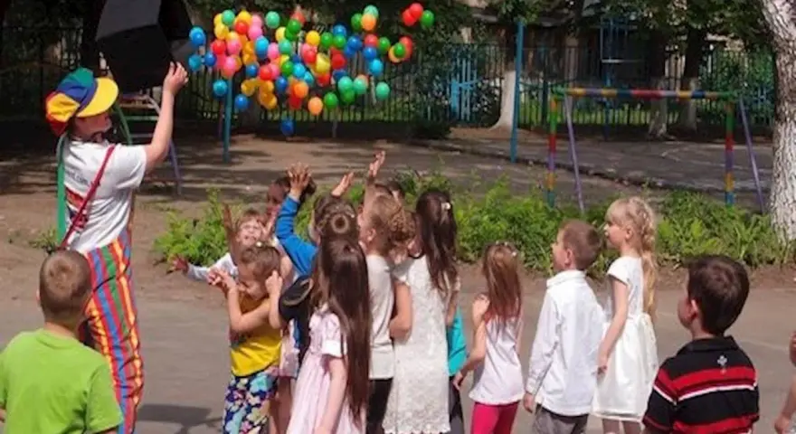 Klaun wypuszcza balony dla dzieci. Czy są zerówki w szkołach? Dzieci cieszą się zabawą na świeżym powietrzu.