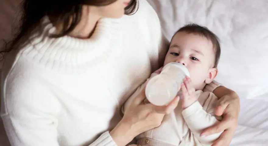 Mama karmi butelką dziecko, które właśnie pije mleko. Ważne jest, ile mleka powinien jeść noworodek.