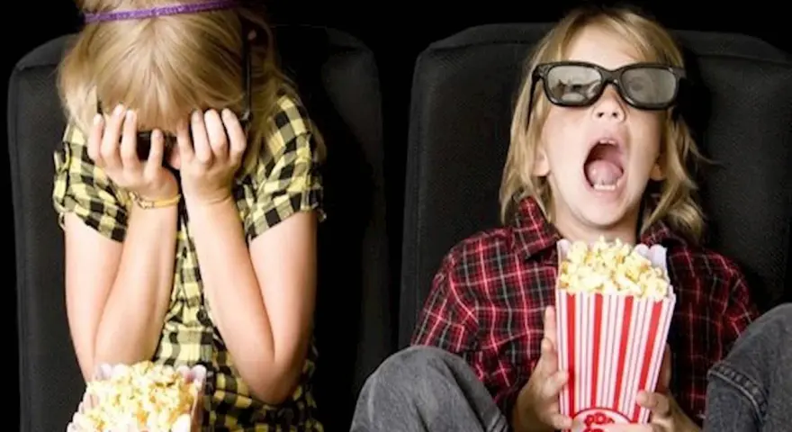 Dzieci w kinie, kiedy pierwszy raz do kina z dzieckiem. Jedno zakrywa twarz, drugie z popcornem w szoku.