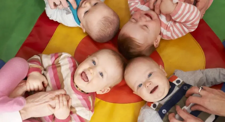 Uśmiechnięte dzieci na kolorowej macie. Czy żłobek jest dobry dla dziecka? Wiele maluchów wesoło bawi się z opiekunami.