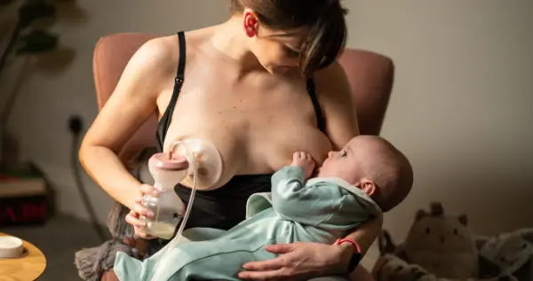 Kobieta karmi piersią dziecko, jednocześnie używając laktatora Tommee Tippee do odciągania mleka.