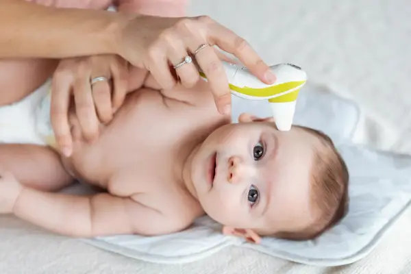 Mama mierzy temperaturę czoła niemowlaka termometrem bezdotykowym. To szybki sposób, gdzie mierzyć temperaturę u niemowlaka.