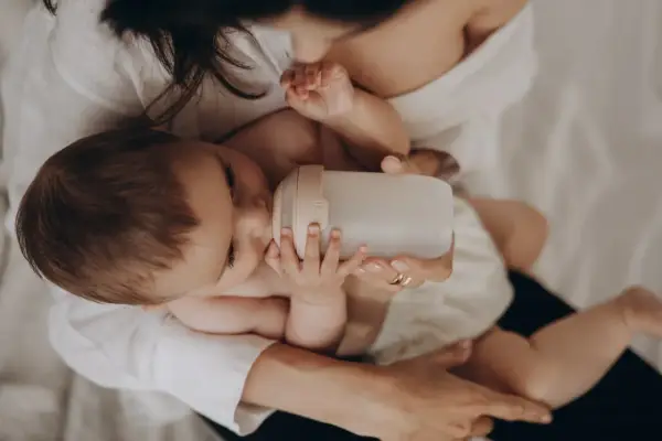 Dziecko pije z butelki przypominającej pierś. Mama czule trzyma butelkę, zapewniając maluchowi komfort.