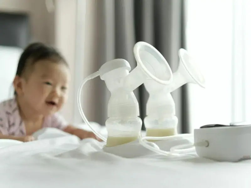 Laktator elektryczny Canpol Babies z butelkami mleka i uśmiechniętym dzieckiem w tle.