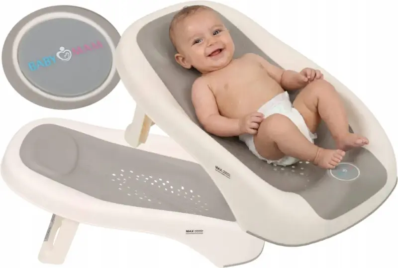 Uśmiechnięty niemowlak w pieluszce leży na leżaczku do kąpieli dla niemowlaka. Produkt BabyMam zapewnia bezpieczeństwo i komfort podczas kąpieli.