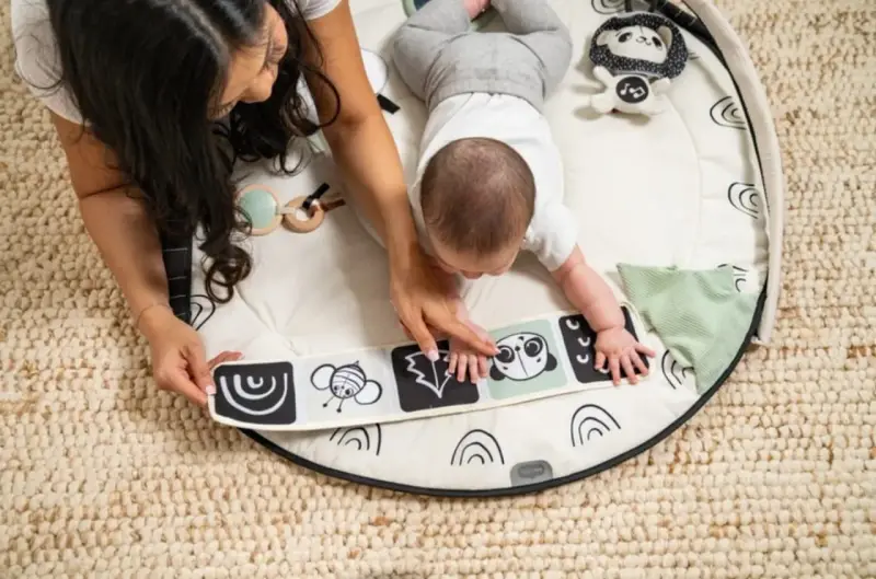 Mama i dziecko odkrywają kontrastową książeczkę na macie edukacyjnej dla niemowlaka Tiny Love.