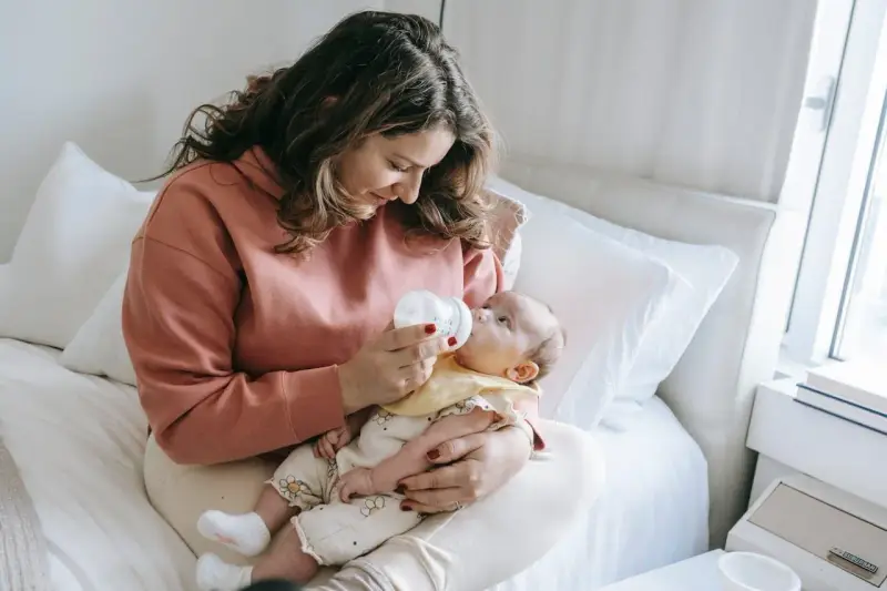 Mama karmi dziecko butelką, używając miarki do mleka modyfikowanego.